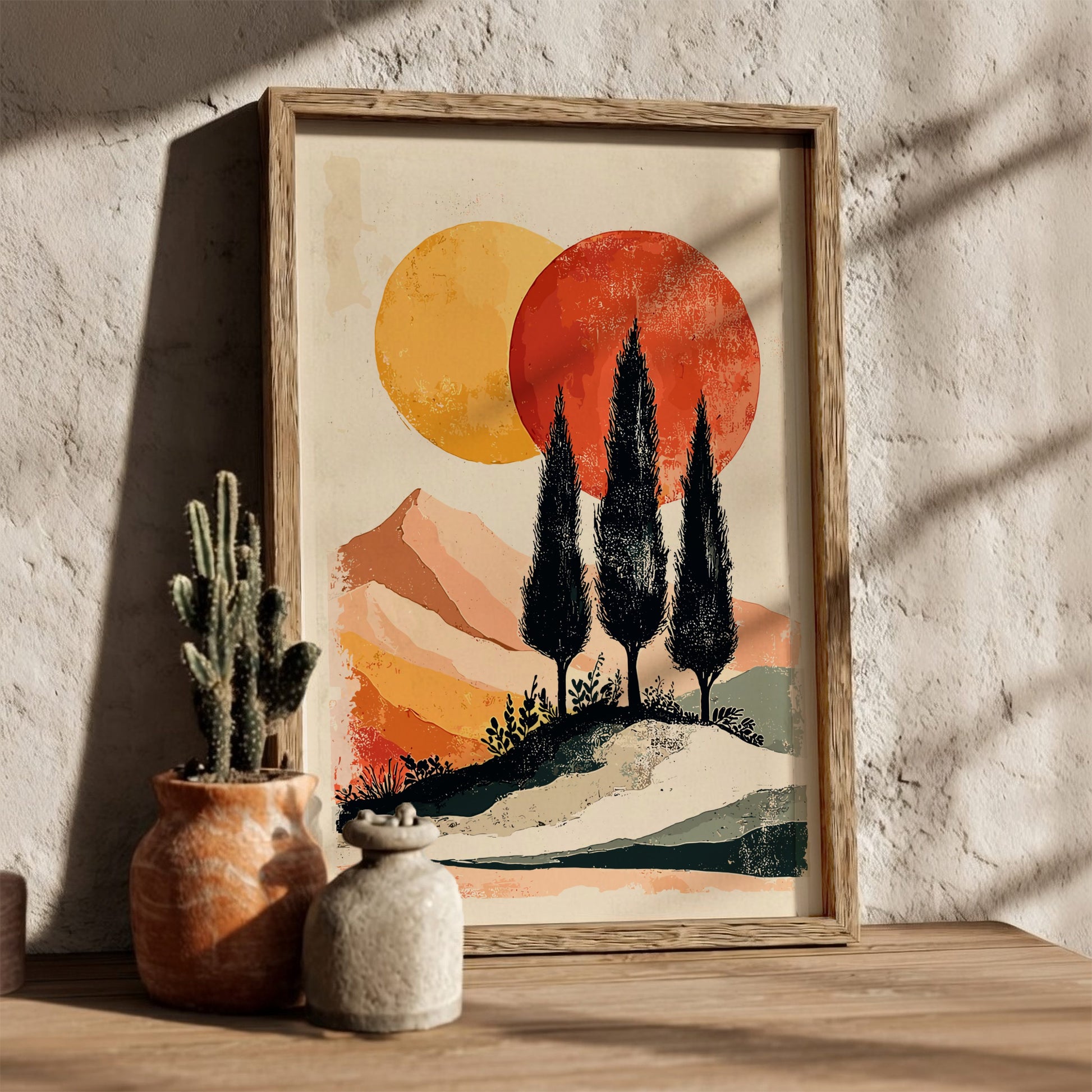 Framed artwork of a sunset with trees and mountains, placed on a wooden surface with decorative pots.