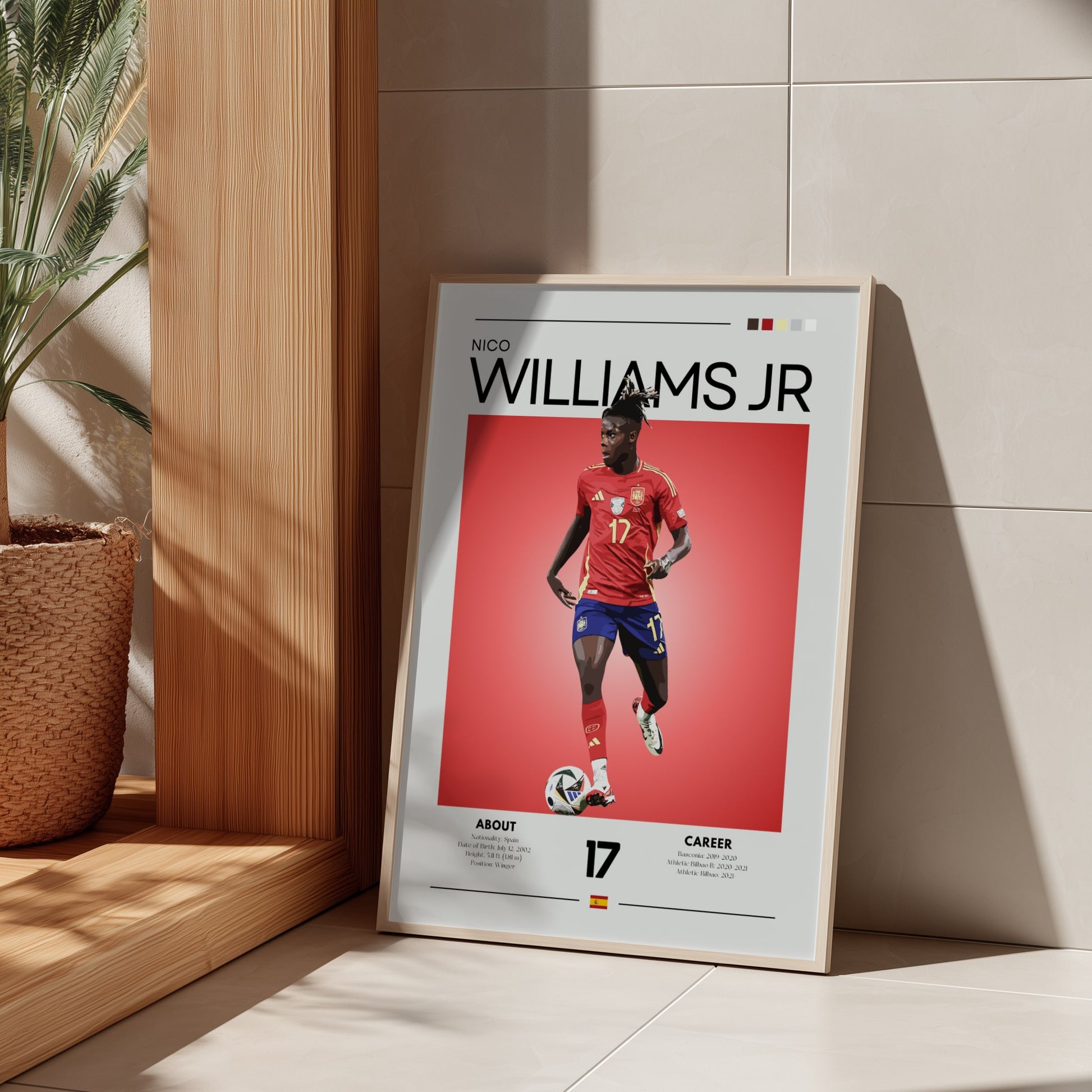 Framed poster of a soccer player with 'Nico Williams Jr.' on a red background, leaning against a wall.
