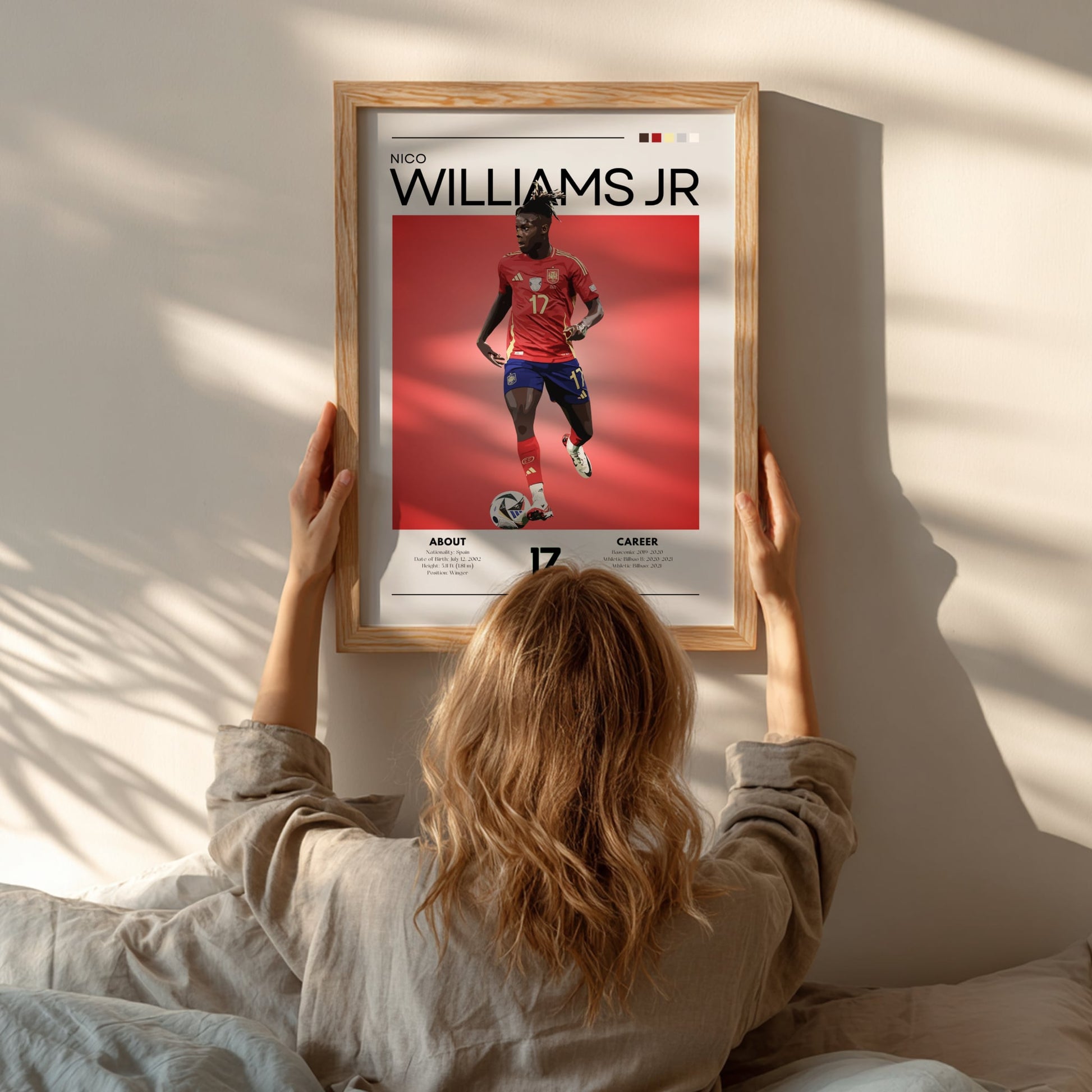 Person hanging a framed poster of a soccer player named Williams Jr. on a wall.