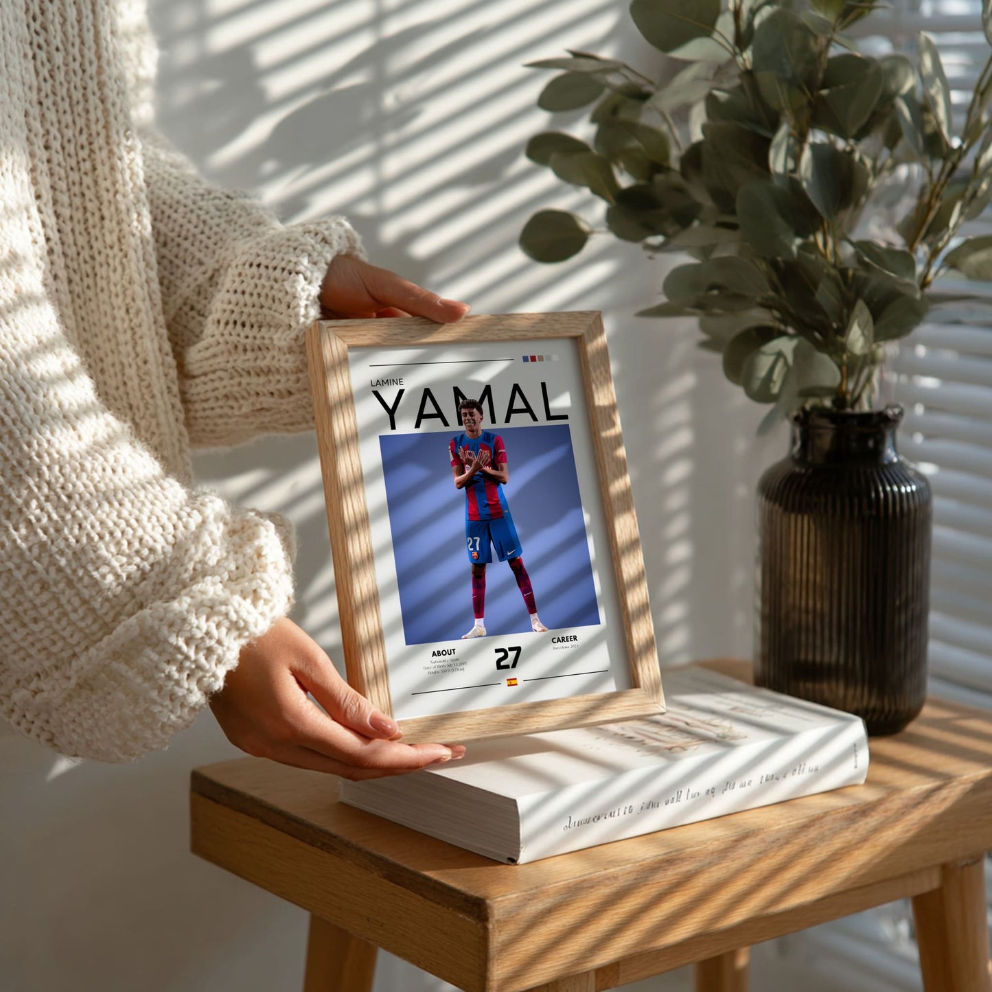 Person holding a wooden photo frame with a picture of a person in sports attire on a table with a plant in the background.