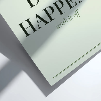 A close-up of a pale sage green paper card or label with black serif text reading 'HAPPEN' and smaller text 'wash it off', shown on a white surface with a soft shadow.