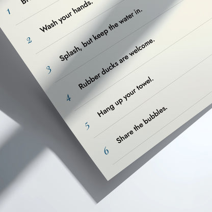 A close-up of a printed instruction sheet showing numbered steps in blue text, including 'Wash your hands,' 'Splash, but keep the water in,' 'Rubber ducks are welcome,' 'Hang up your towel,' 'Share the bubbles,' on a white background with a soft shadow.