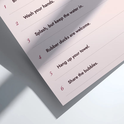A close-up of a printed instruction sheet showing numbered steps in red text, including 'Wash your hands,' 'Splash, but keep the water in,' 'Rubber ducks are welcome,' 'Hang up your towel,' and 'Share the bubbles.' The sheet is photographed at an angle on a clean white surface with soft shadows.