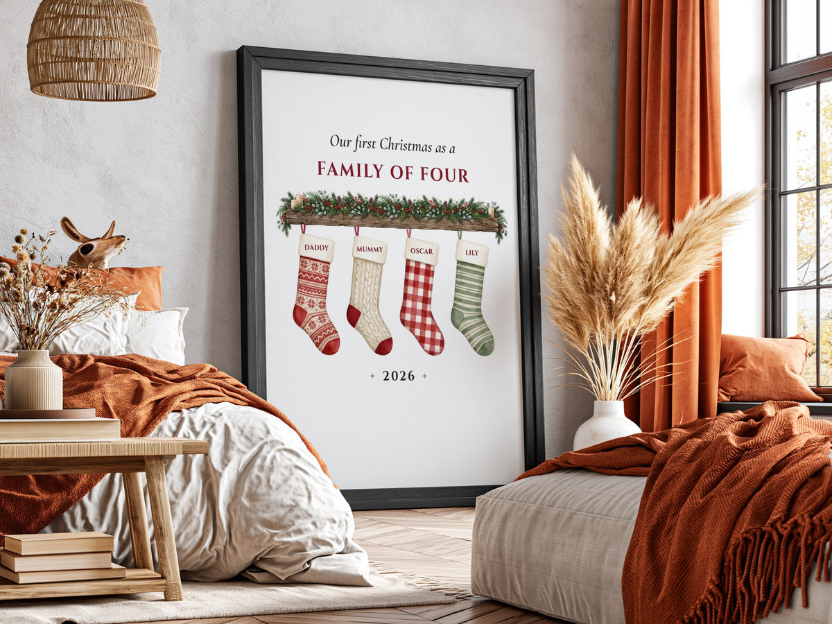 A framed personalized Christmas print leaning against a wall in a styled bedroom. The print reads 'Our free Christmas as a FAMILY OF FOUR' above four colorful Christmas stockings, with '2026' at the bottom.