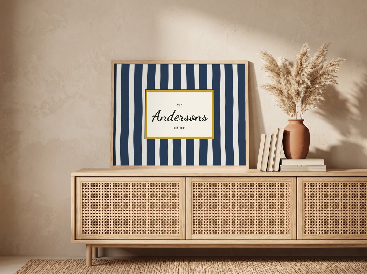 A framed personalized art print with navy and white vertical stripes and a gold border, featuring the text 'The Anderssons EST. 2021' in black script.
