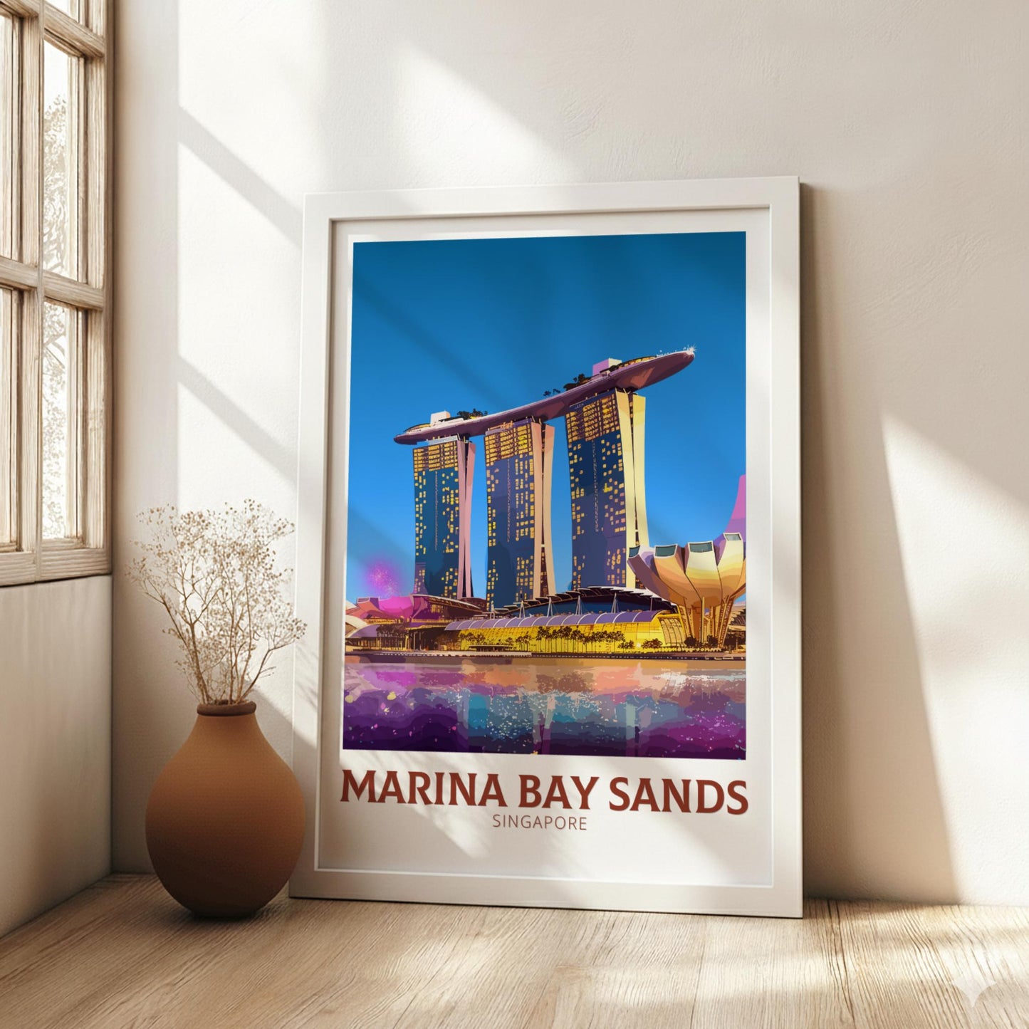 Framed poster of Marina Bay Sands in Singapore on a wall with a vase and plant below.