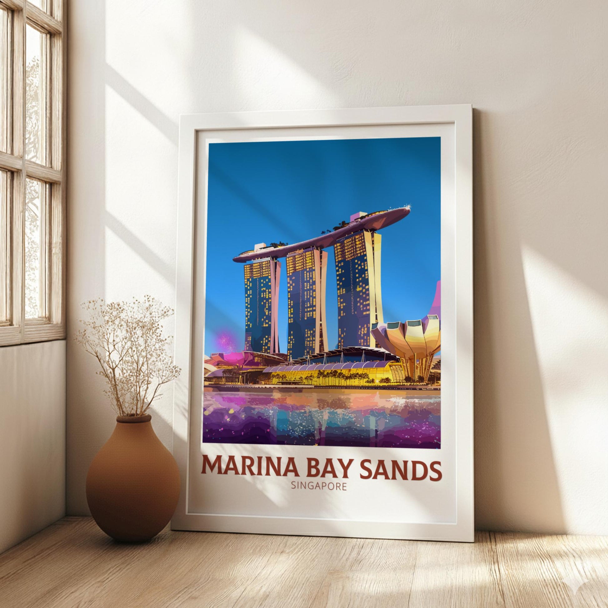 Framed poster of Marina Bay Sands in Singapore on a wall with a vase and plant below.