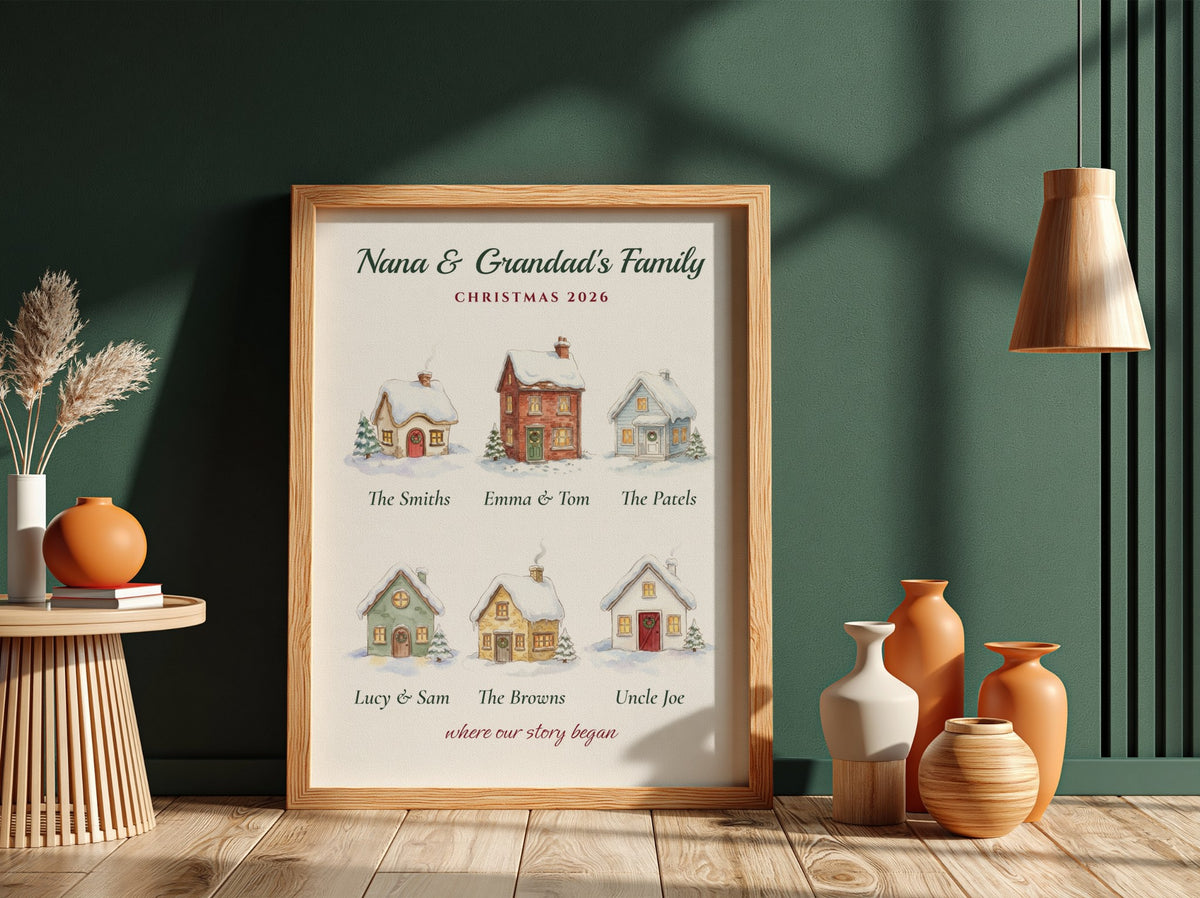 A personalized framed Christmas family print leaning against a dark green wall on a wooden floor, surrounded by decorative vases, a side table, and a hanging lamp.