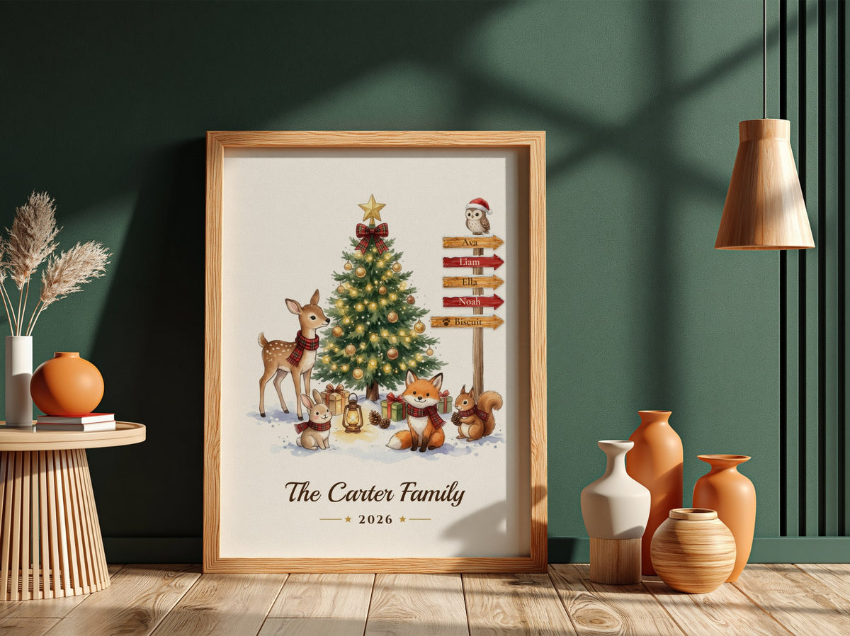 A framed personalized Christmas art print featuring a decorated tree, woodland animals, and a signpost, displayed in a styled room with a dark green wall, wooden floor, side table, and vases.
